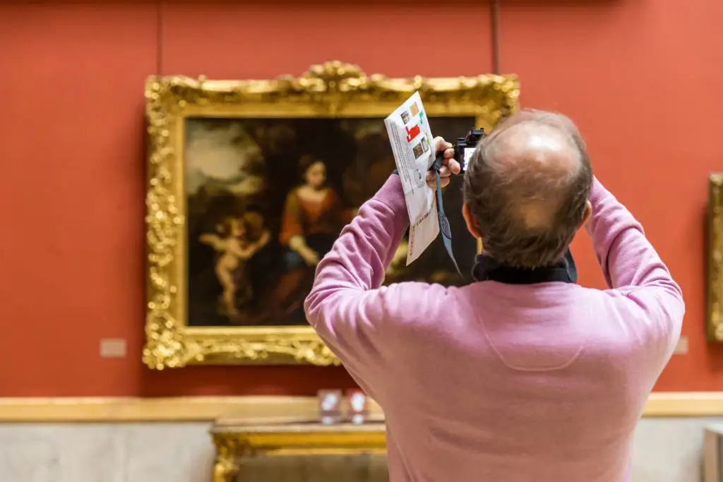 Tourist with DSLR taking a photo having learned how to photograph paintings in a museum