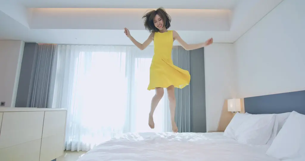 Woman jumping on bed in a yellow dress.