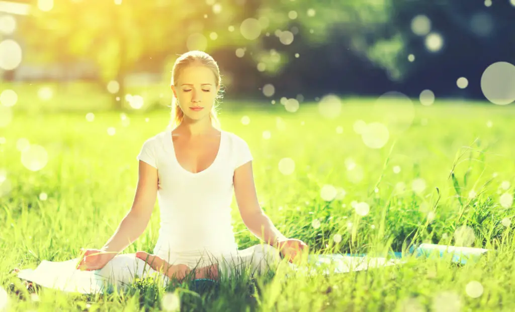 Woman meditating in a grassy meadow.