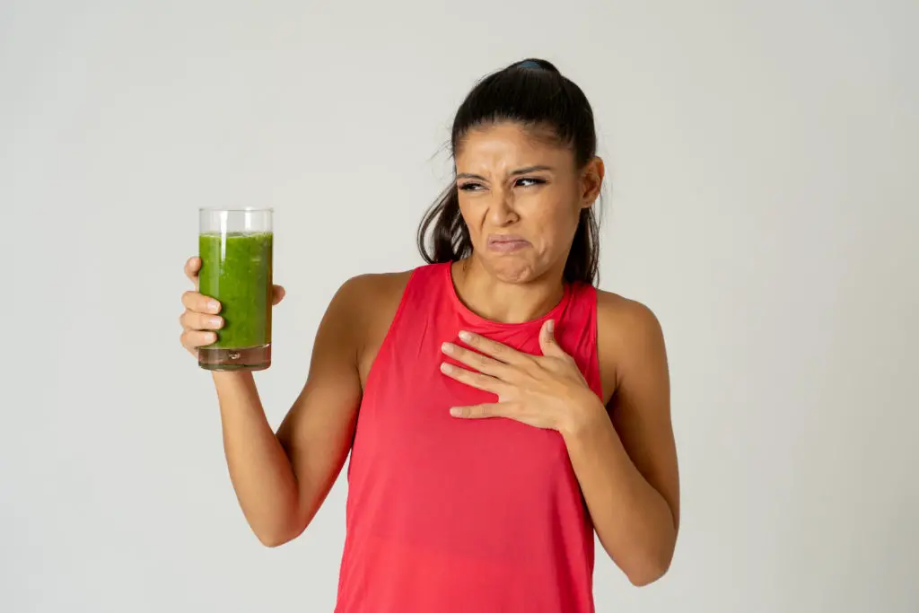 Woman tasting a disgusting green smoothie to try to spark creativity.