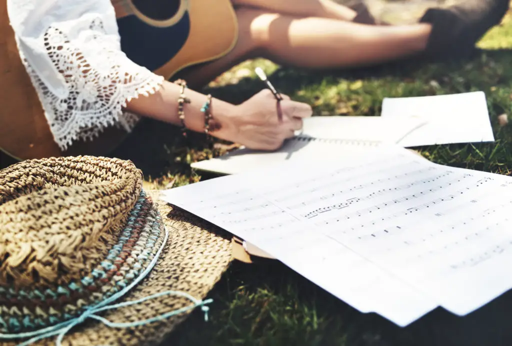 Hippie girl writing songs with acoustic guitar in park.