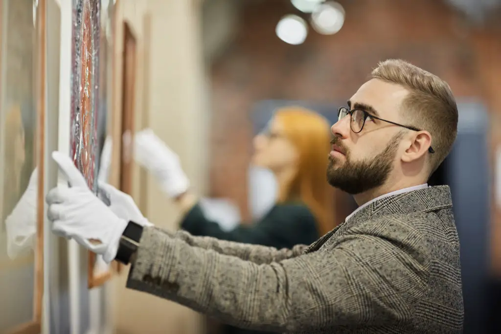 Man with white gloves hanging a canvas who knows how to handle artwork