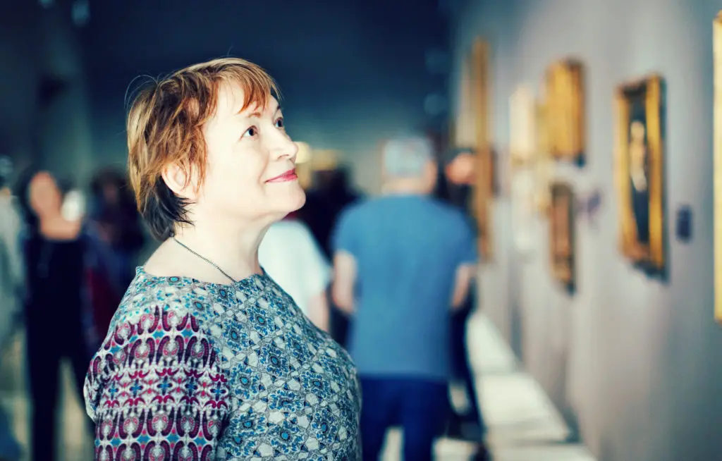 Older woman looking at paintings in a museum.