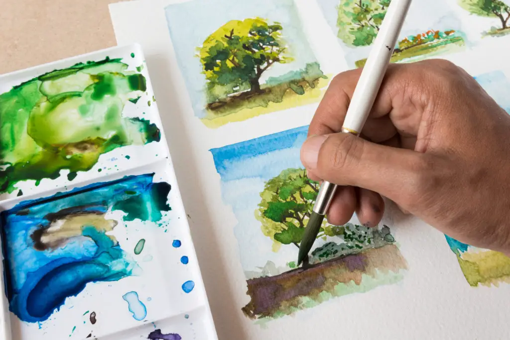 Close up of an artist carefully painting a tree with watercolor.