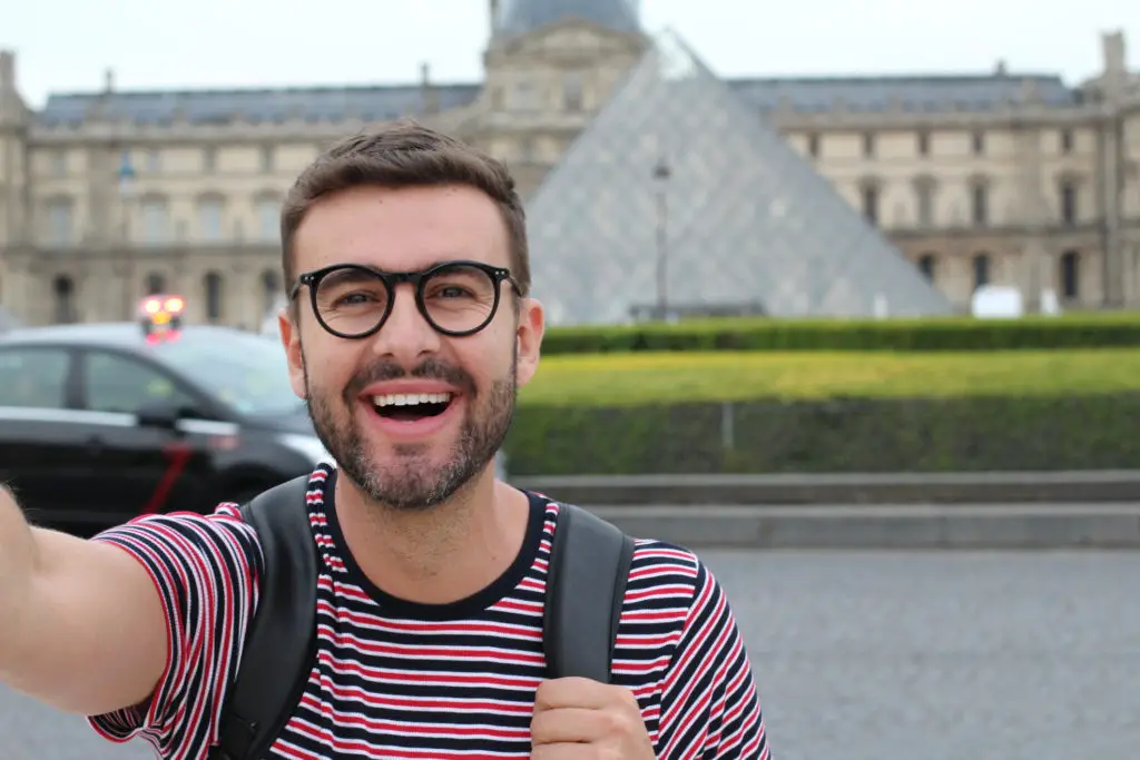 Man with backpack in front of The Louvre Museum starting his tour of the best Paris art galleries and museums