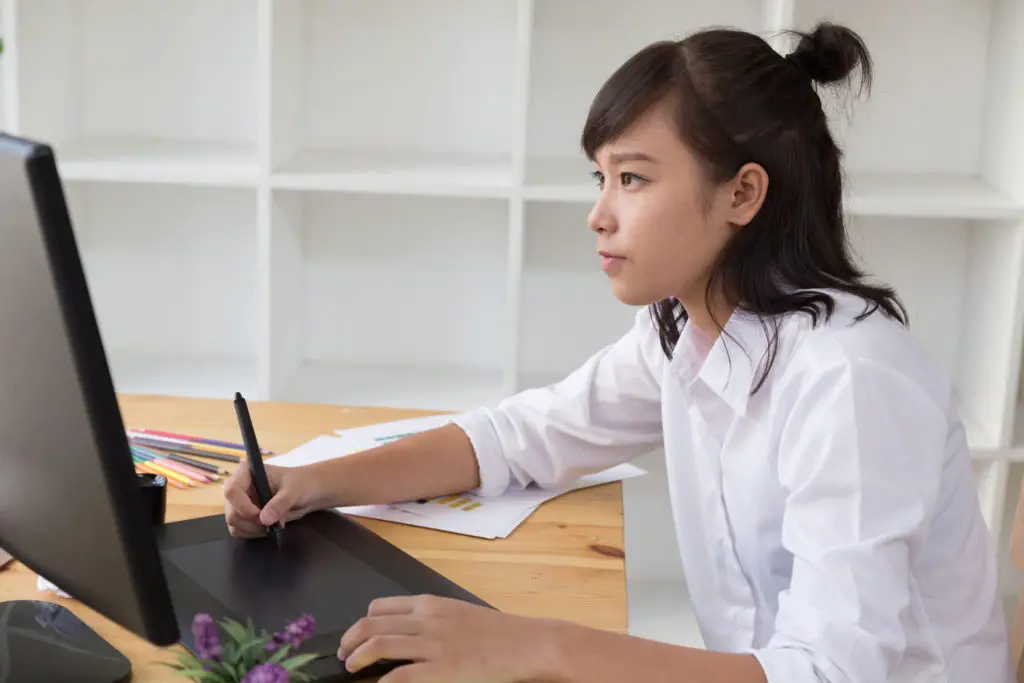 Woman at desk using digital drawing tablet creating artwork for her art patron