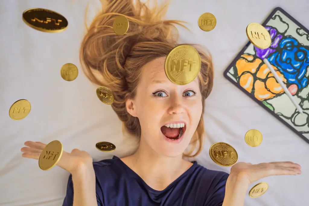 Young woman, a digital artist, creates digital art on a tablet at home and shows a coin with the inscription NTF - non fungible token.