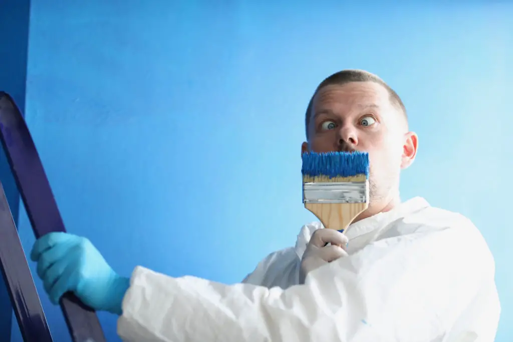 Male painter holds paintbrush near his face.