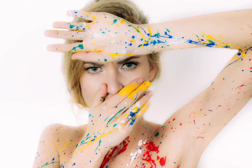 Woman covering her nose while covered in oil paint splatters.
