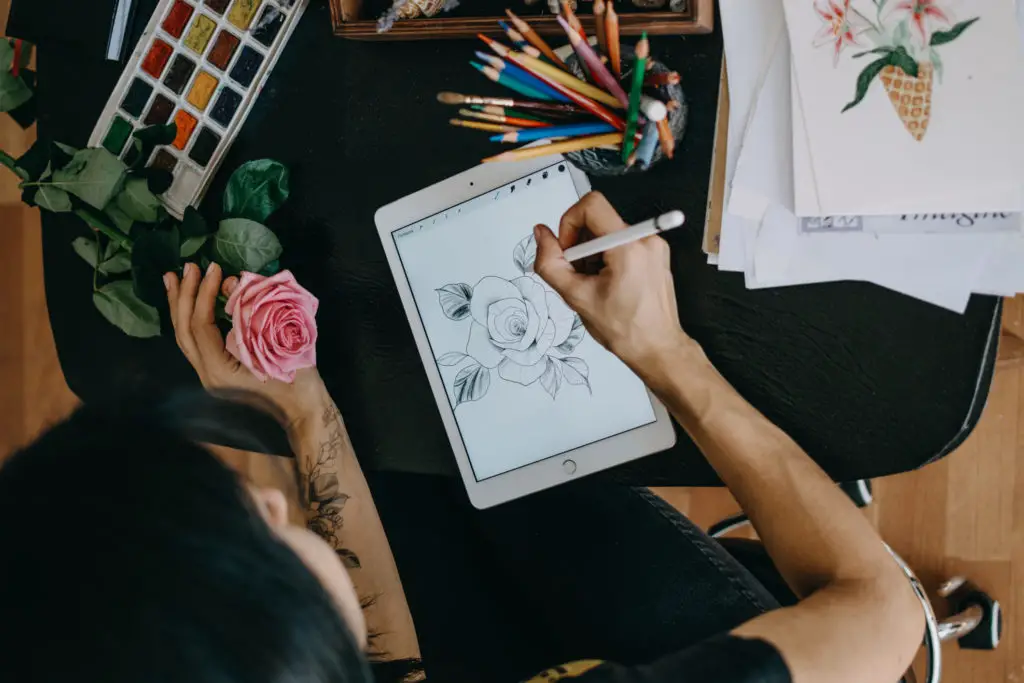 Artist with tattoos drawing a realistic rose using Apple Pencil on an IPad.