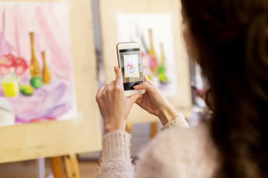 Woman using her smartphone to photograph hand drawn art to make into an NFT.