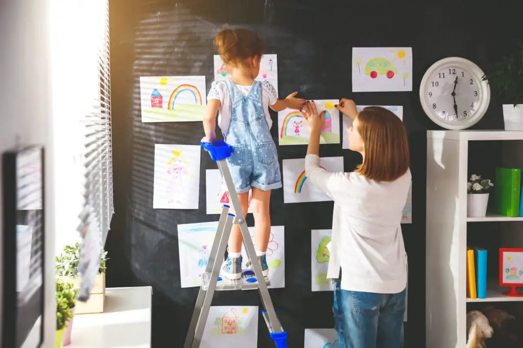 Mother and child hang paper artwork on the wall without damaging the paint.