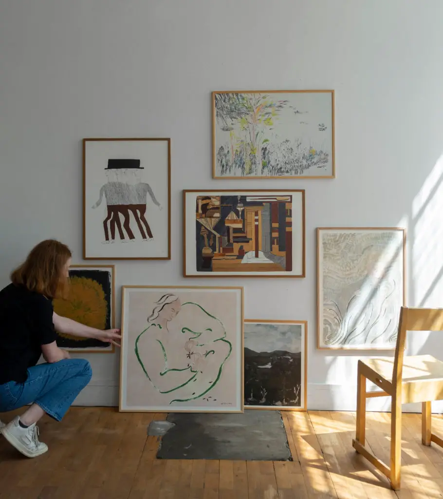 Woman arranging art on a wall and leaning some art against the wall.