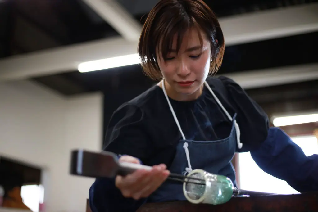 Female glass  artist working on a blown piece in a hot shop.